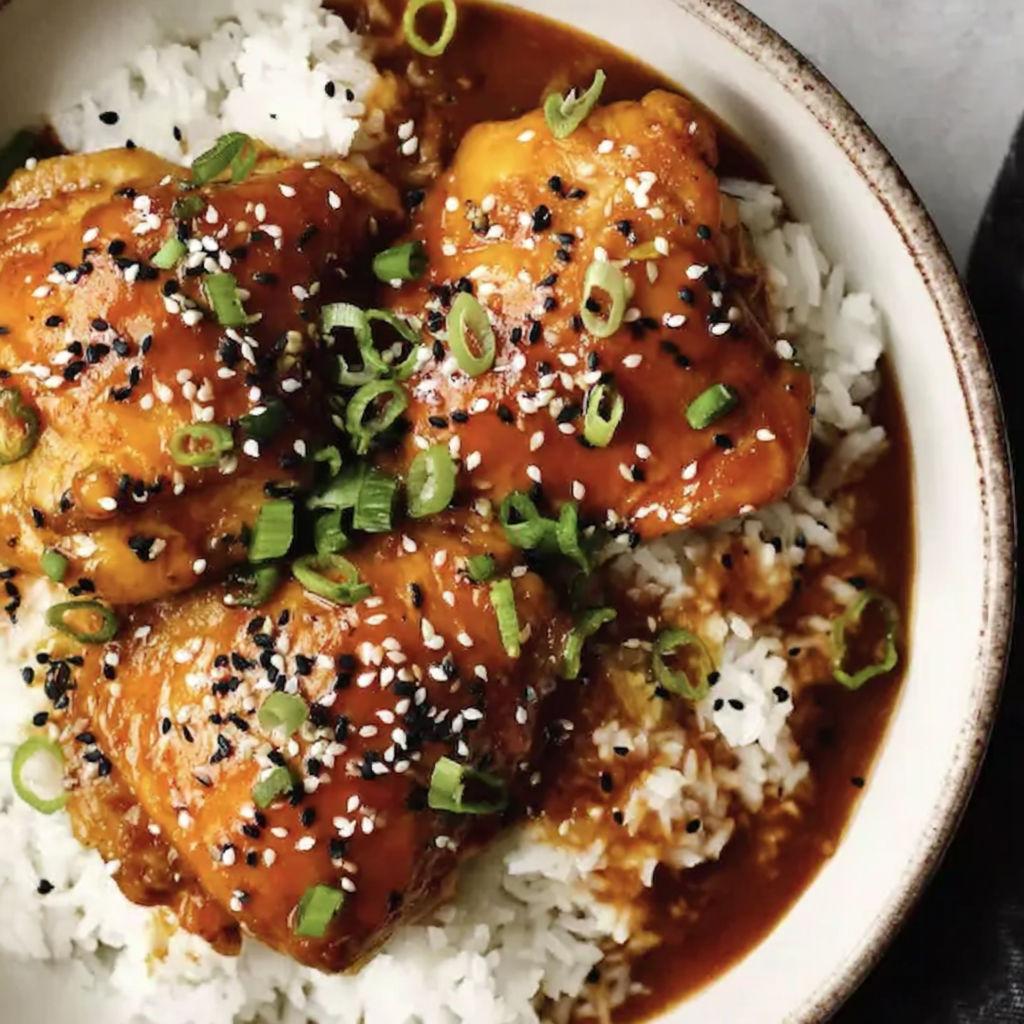 A bowl of rice with chicken thighs and sauce.