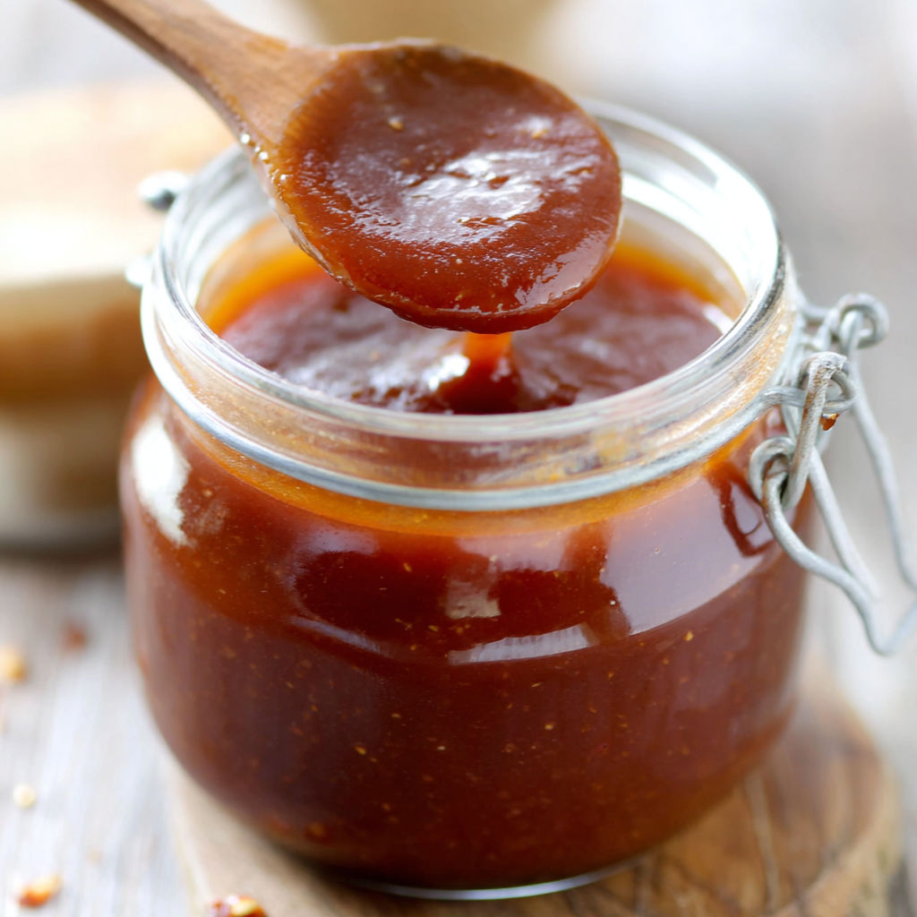 A jar of homemade BBQ sauce being poured into a bowl.