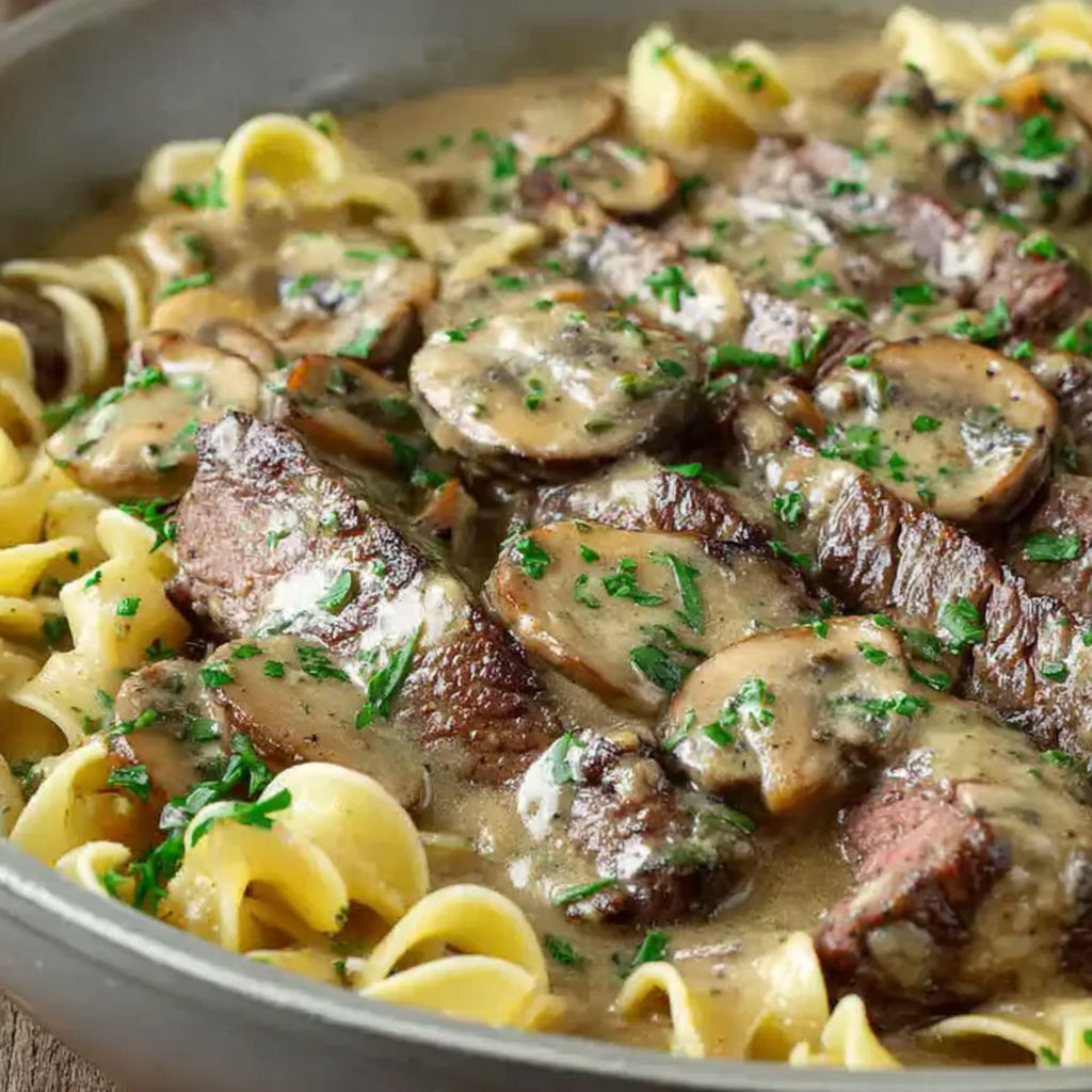 A bowl of beef stroganoff with mushrooms and noodles.