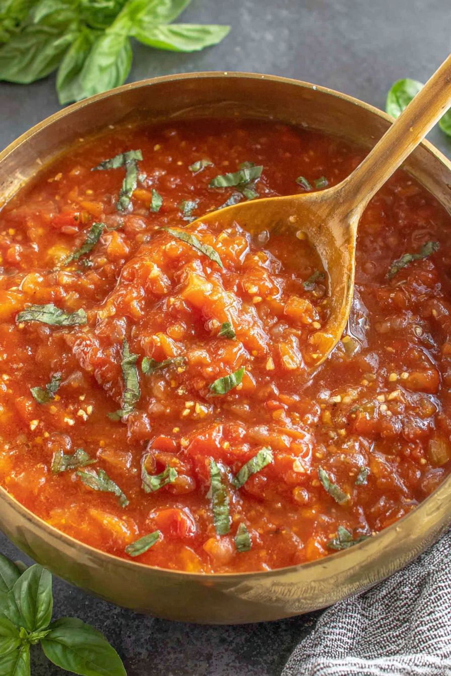 A spoon in a bowl of tomato sauce.