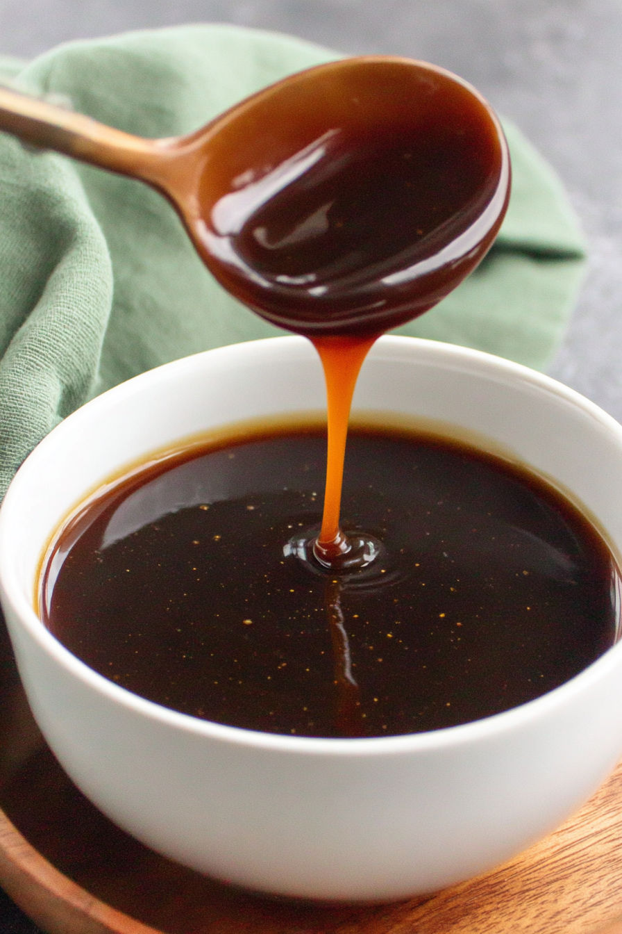 A spoon is pouring teriyaki sauce into a bowl.