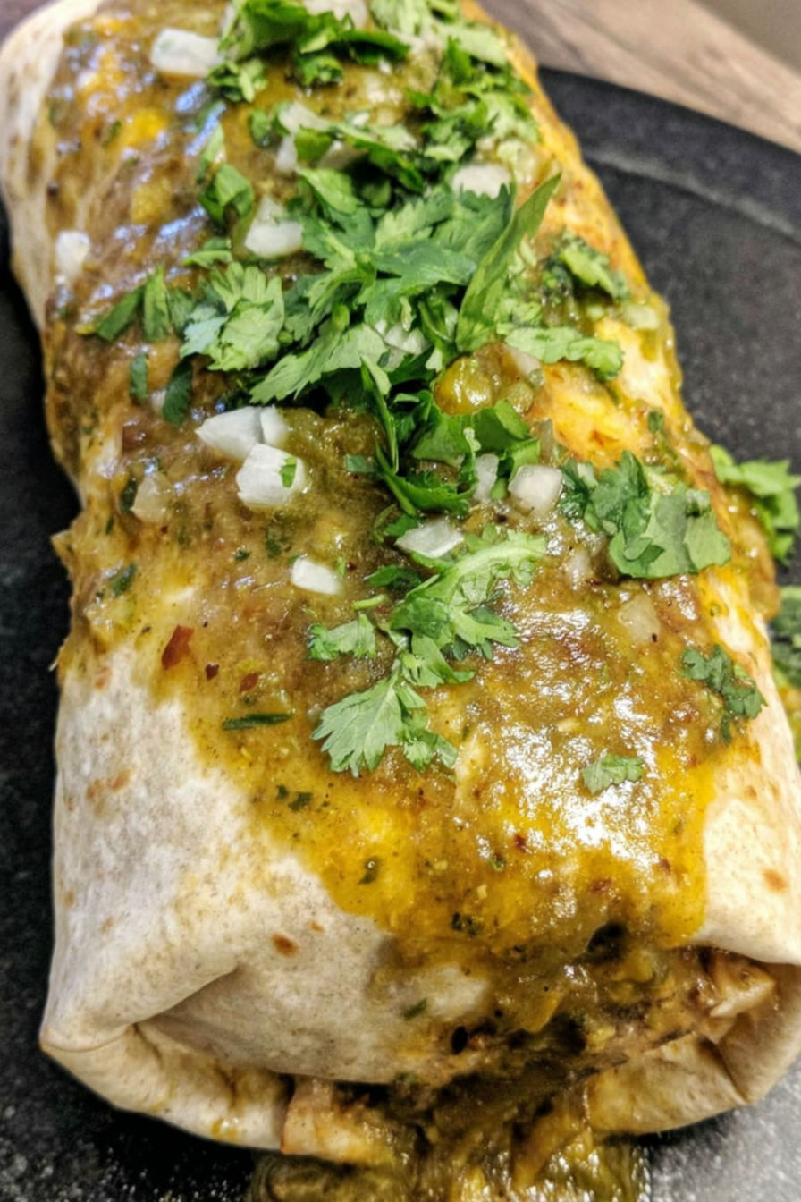 A chili verde hatch burrito with green onions on top.