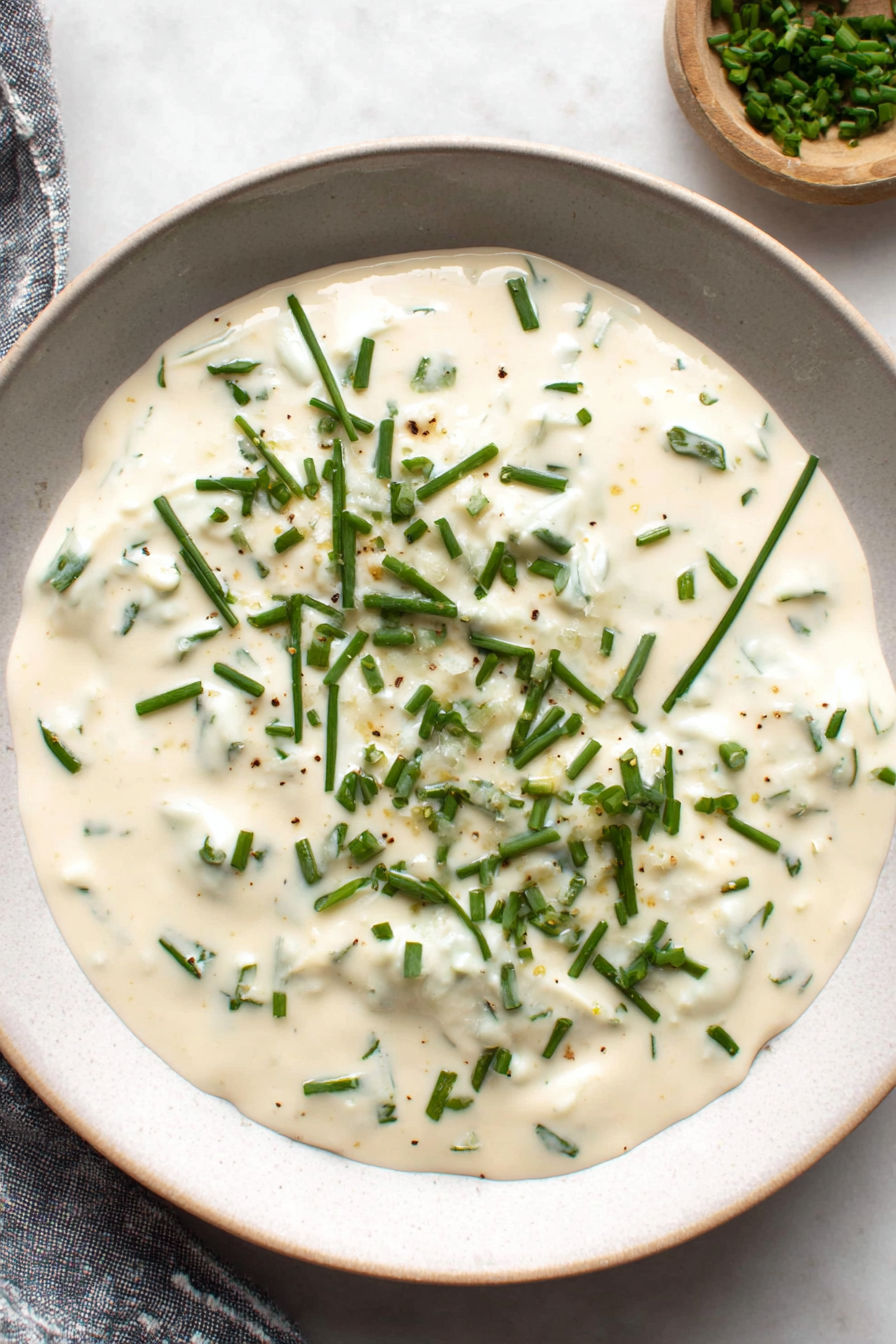 A bowl of creamy horseradish sauce with green herbs.
