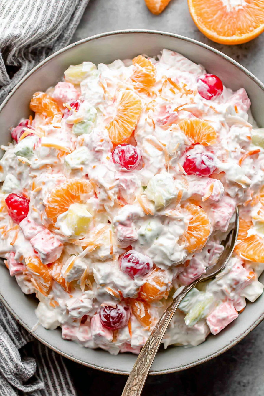A bowl of fruit salad with oranges, cherries, and other fruits.