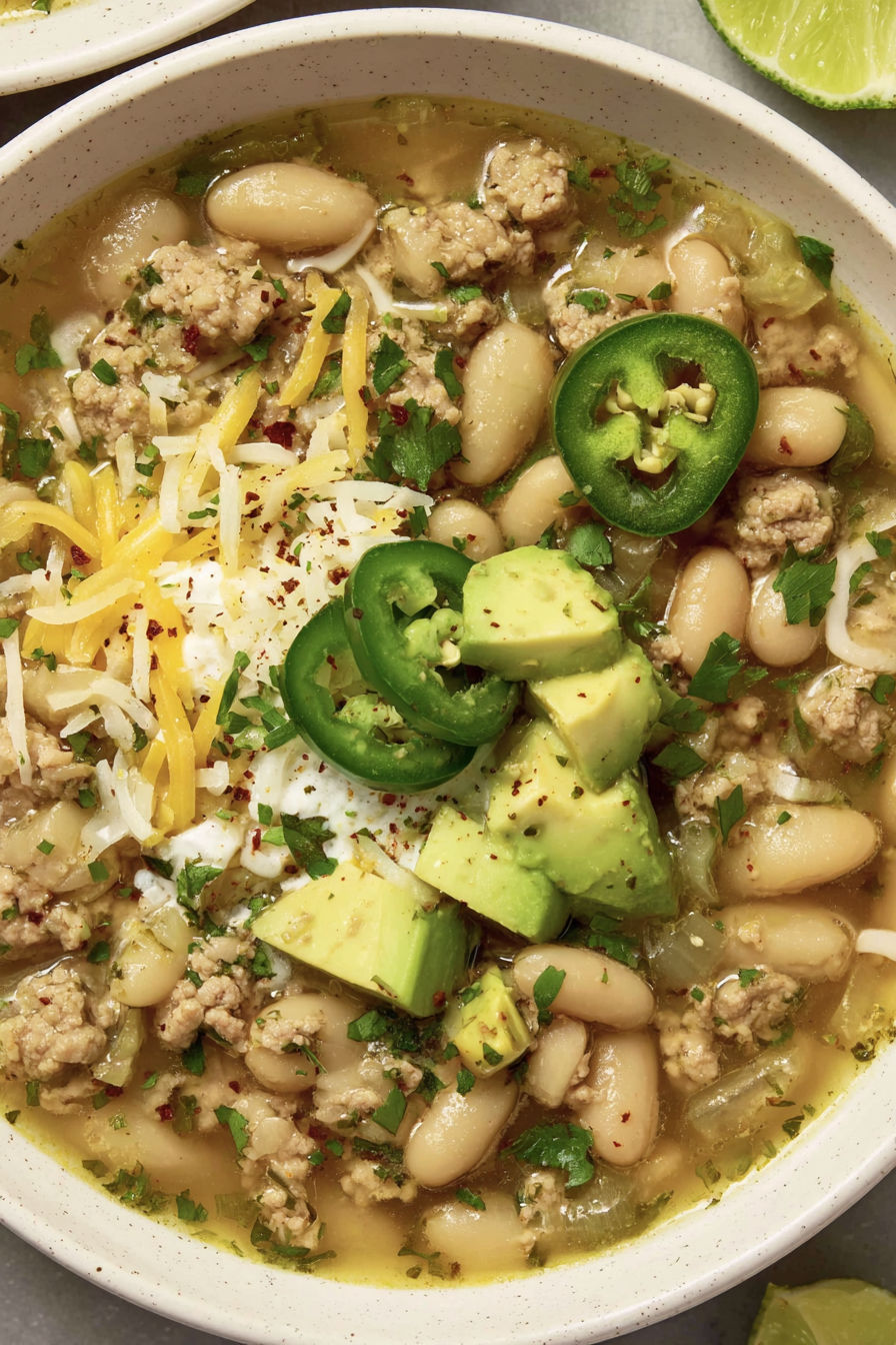 A bowl of chili with avocado, beans, and meat.