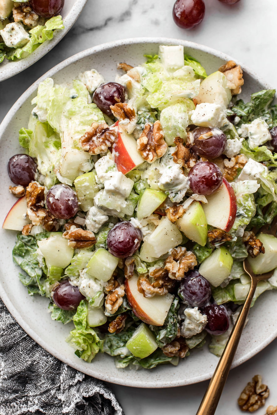 A salad with lettuce, apples, walnuts, and grapes.