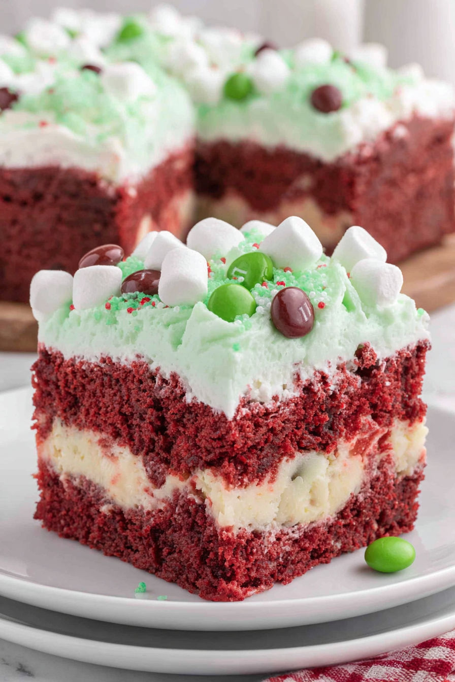 A slice of red velvet cake with white frosting and green candy toppings.