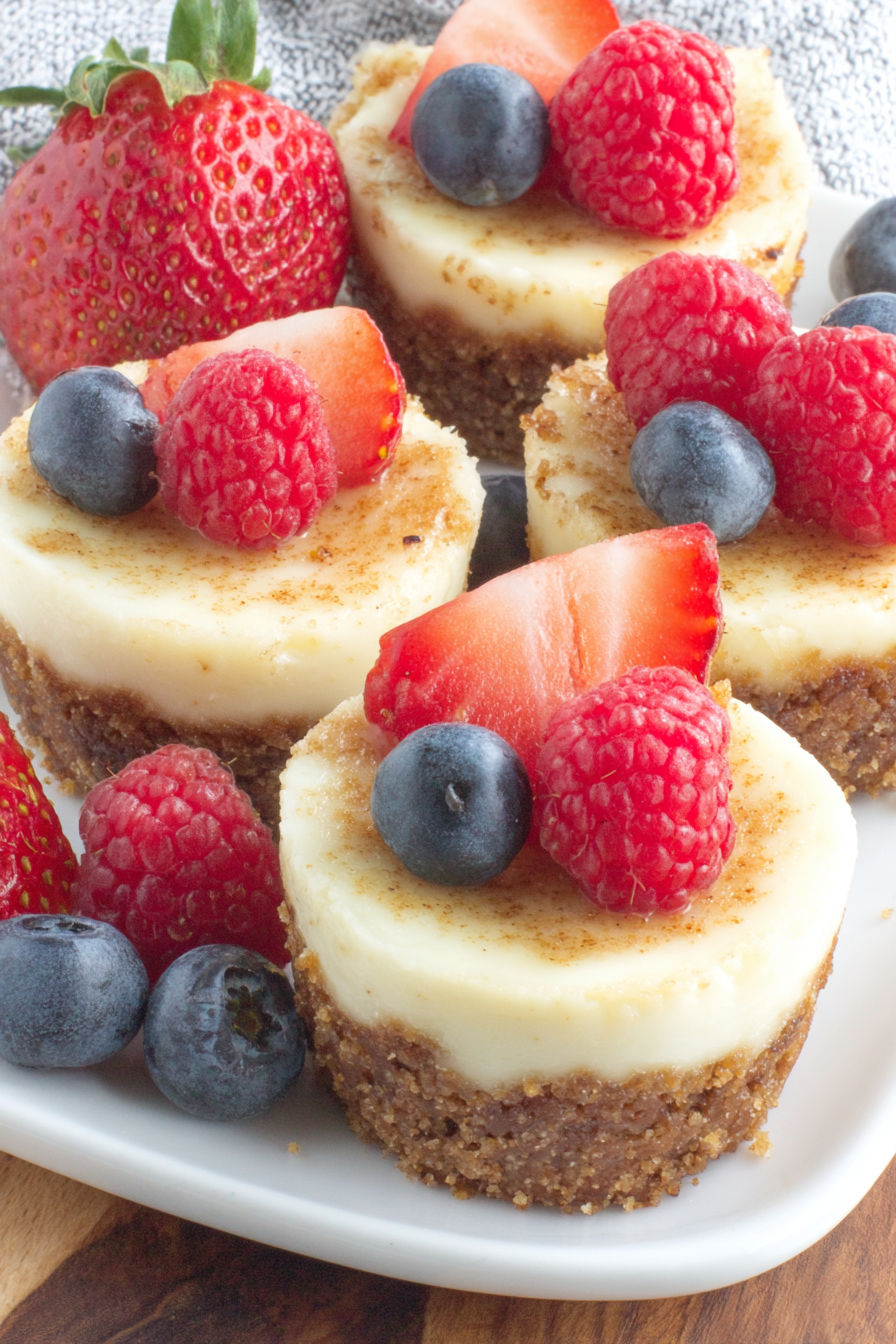 A plate of mini cheesecake bites with strawberries and blueberries on top.