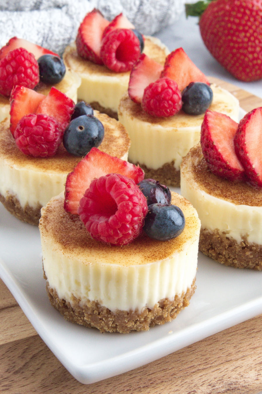 A plate of mini cheesecake bites with berries on top.