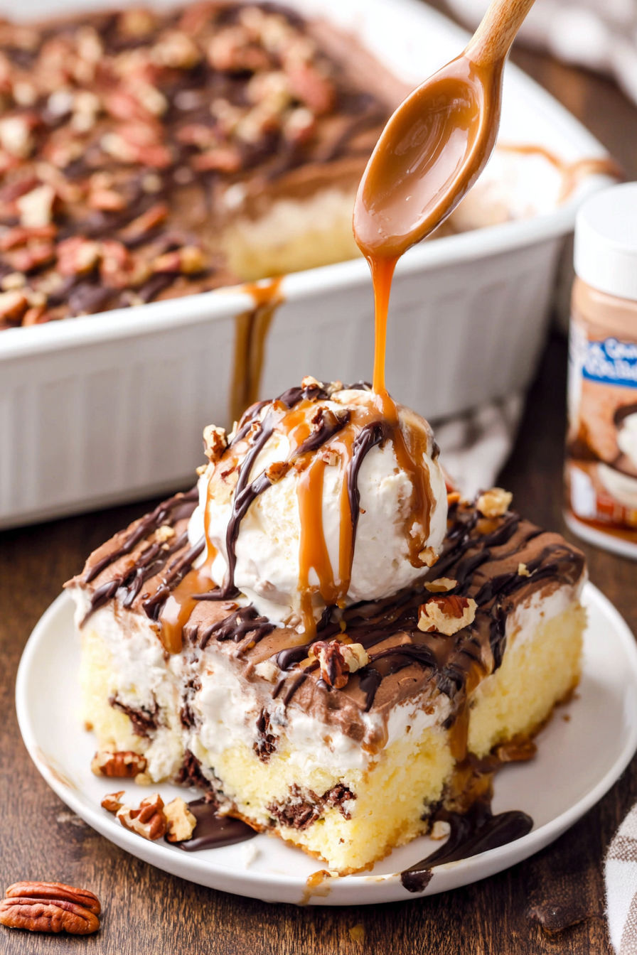 A slice of turtle poke cake with caramel drizzled on top.