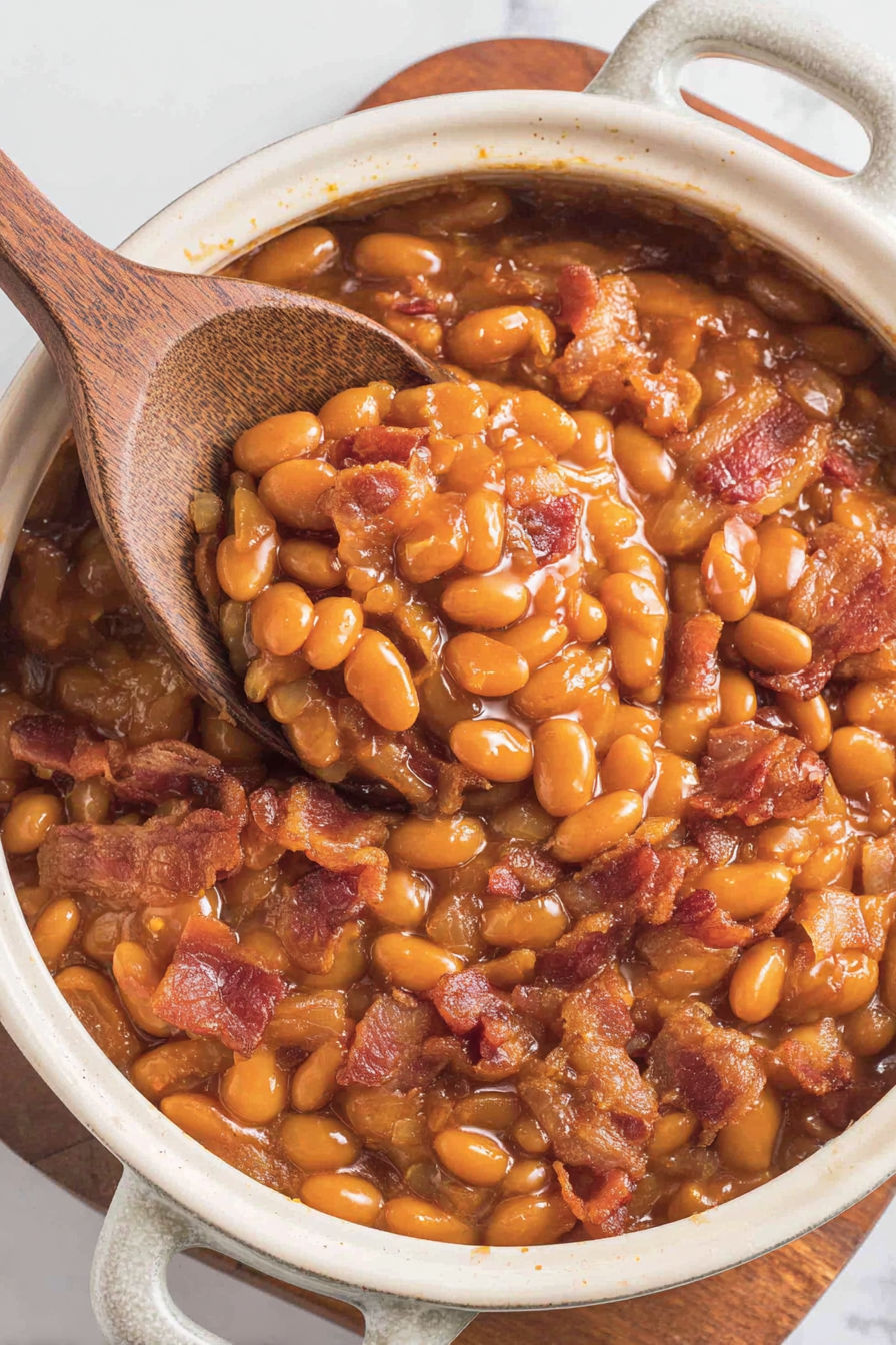 A wooden spoon is in a bowl of baked beans.