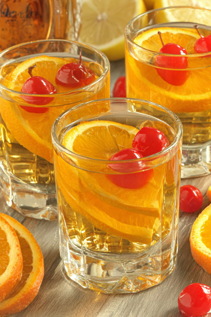 Three glasses of orange juice with cherries on top.