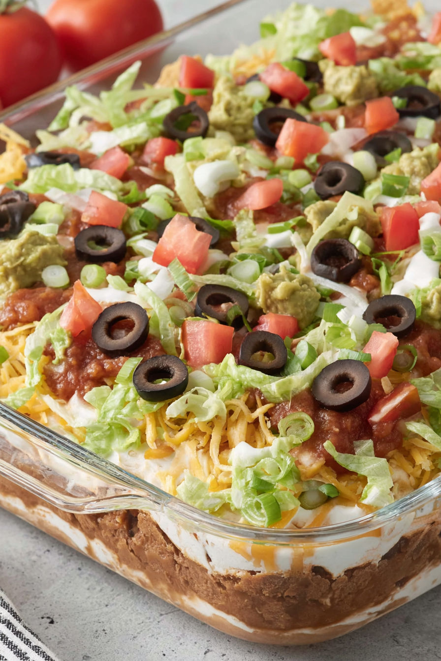 A dish of 7 layer dip with tomatoes and olives.