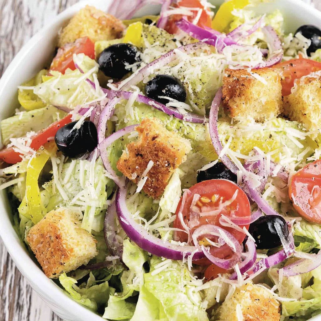A salad with bread croutons, tomatoes, onions, olives, and cheese.