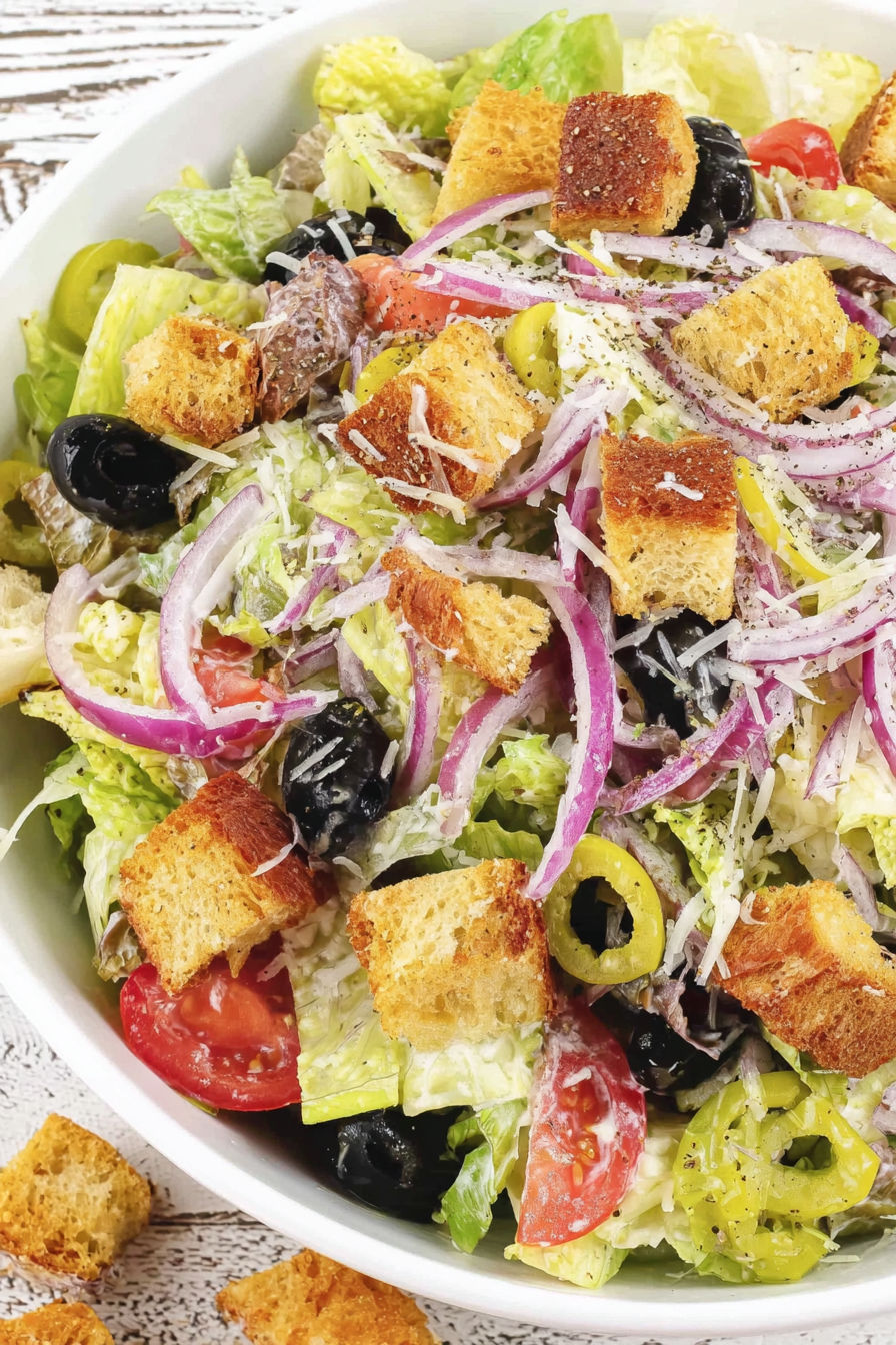A salad with bread, tomatoes, olives, and onions.