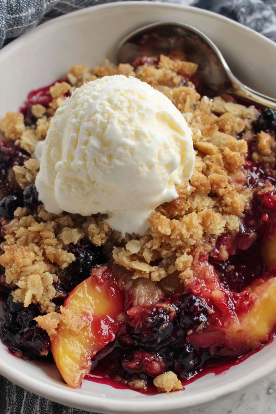 A bowl of blueberry peach crisp with a scoop of ice cream on top.