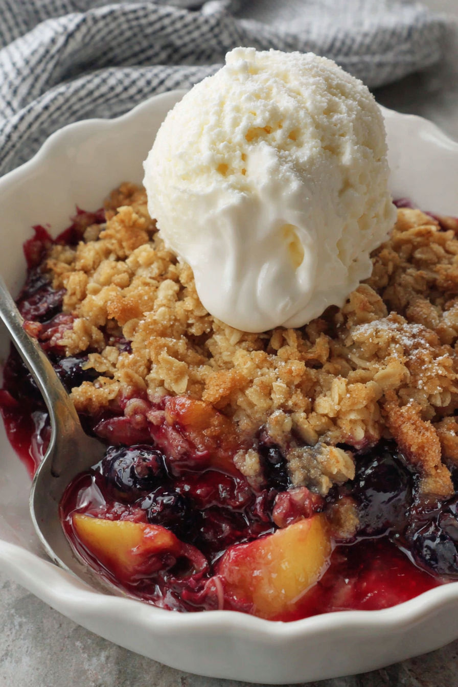 A bowl of blueberry peach crisp with a scoop of ice cream on top.