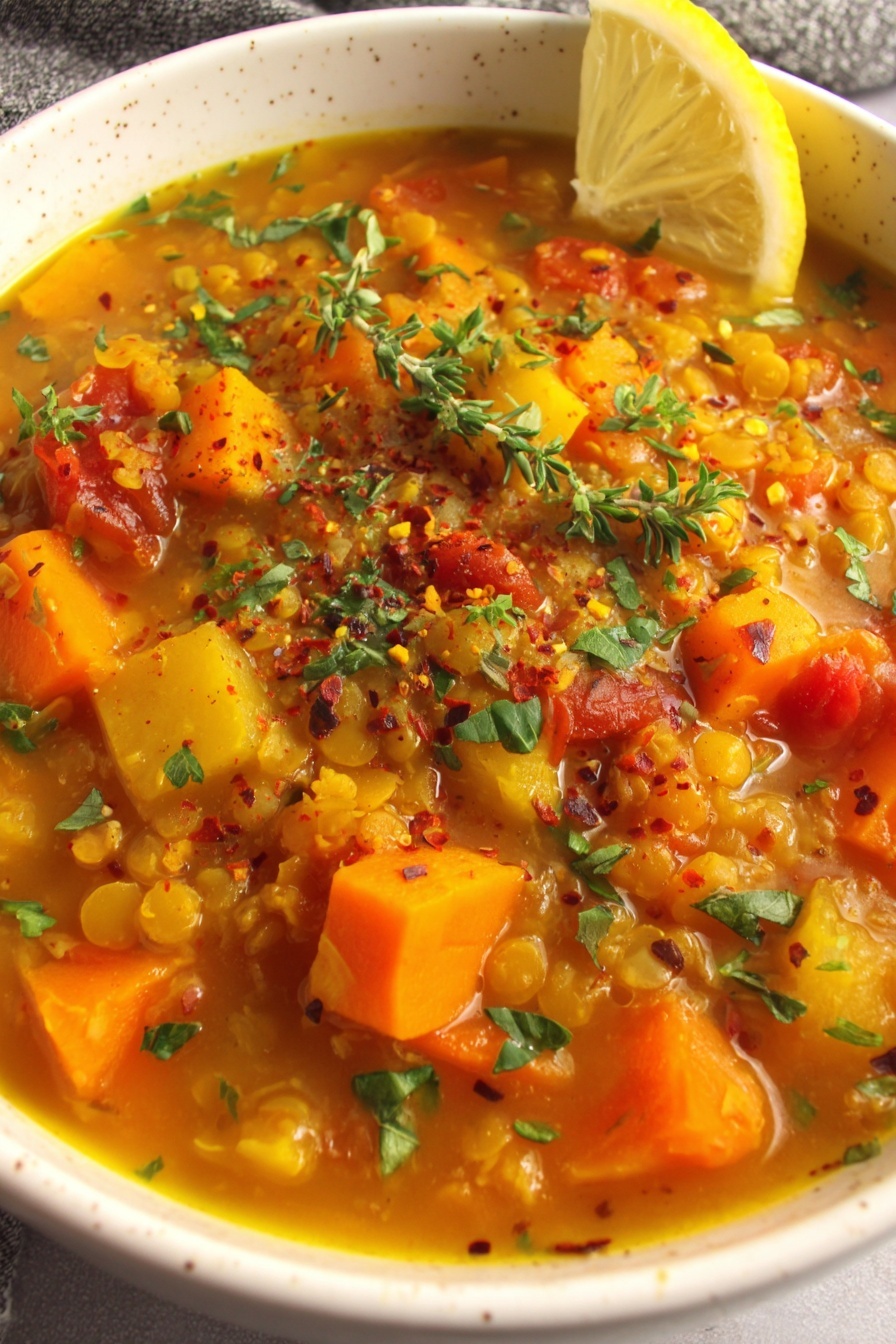 A bowl of red lentil soup with vegetables and herbs.