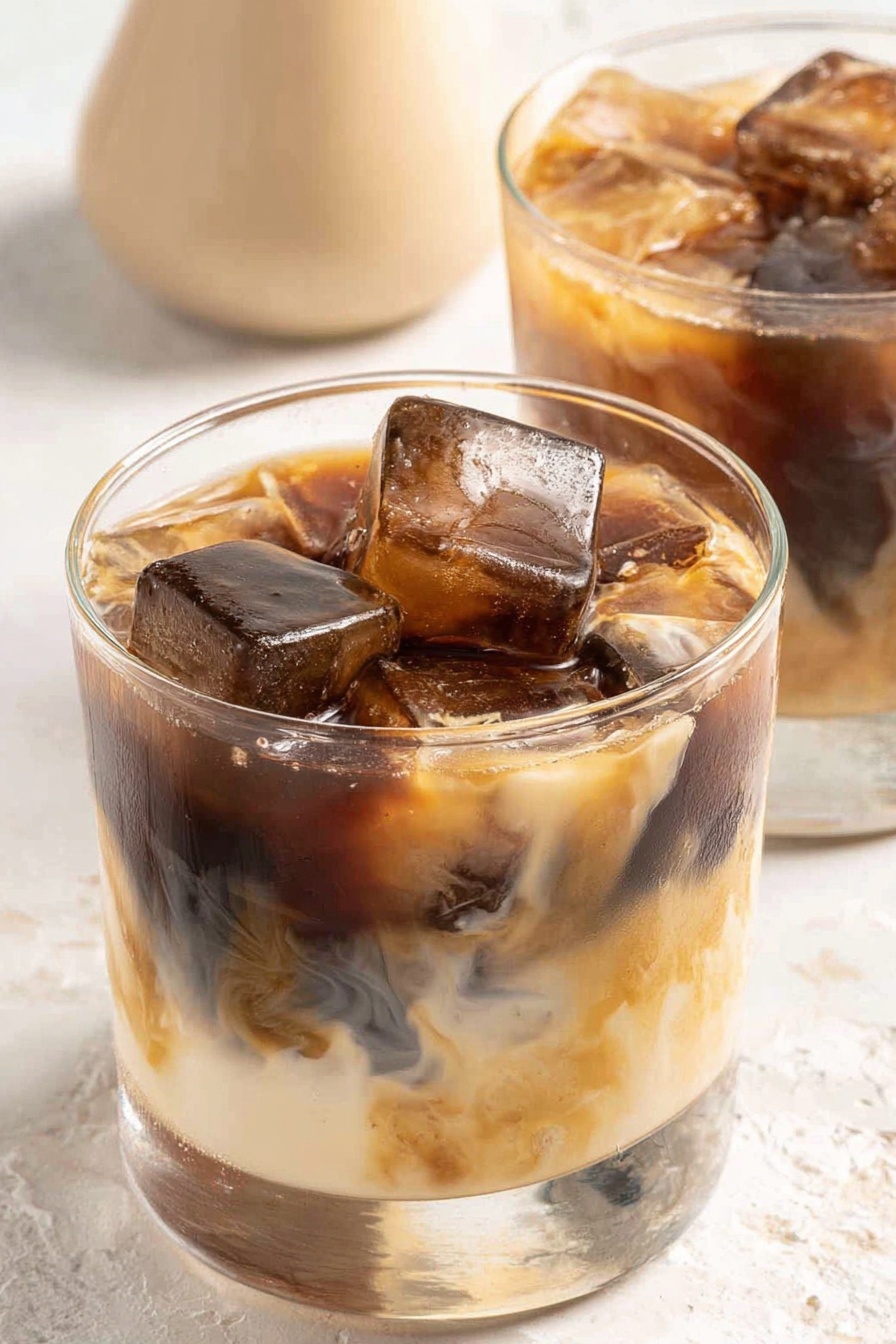 A glass of coffee with ice cubes in it.