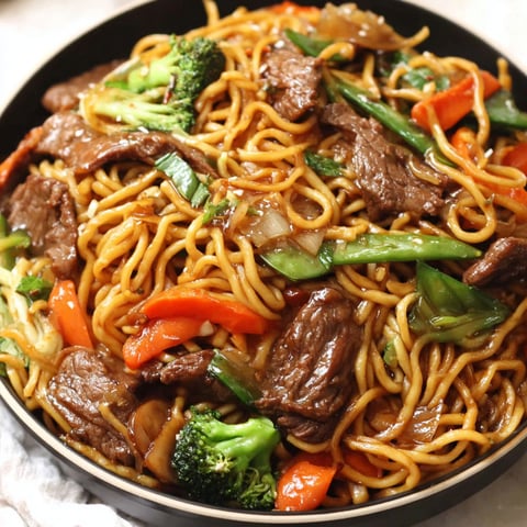A bowl of beef lo mein noodles with vegetables.