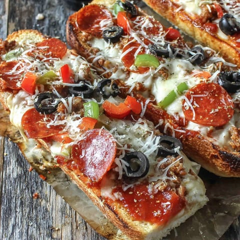 Two slices of grilled French bread pizza with pepperoni and black olives.
