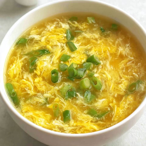 A bowl of soup with green onions in it.