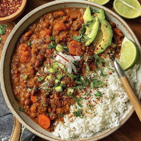 A bowl of vegan chili with rice and lime wedges.