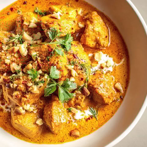 A bowl of chicken korma with nuts and spices.