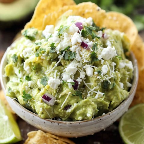 A bowl of guacamole with chips on the side.