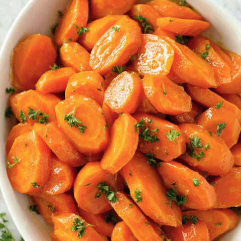 A bowl of carrots with green herbs on top.