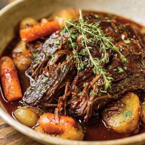 A pot roast with vegetables in a brown bowl.