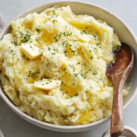 A bowl of mashed potatoes with green herbs on top.