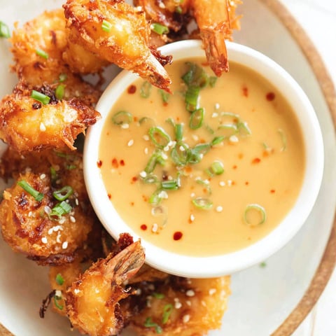A bowl of sauce with shrimp and green onions.