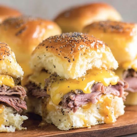 Four roast beef sliders on a wooden platter.