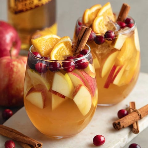 Two glasses of fruit drink with cinnamon sticks in them.