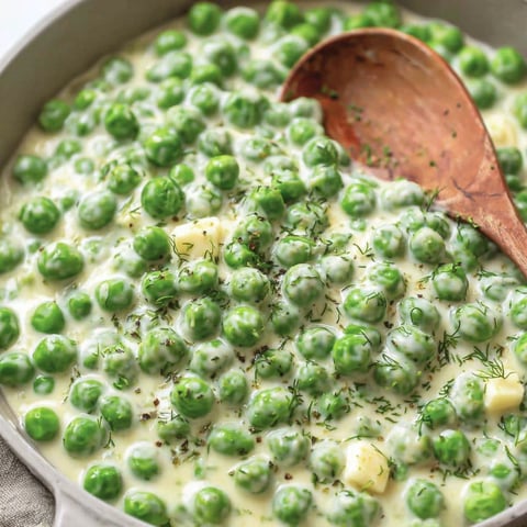 A bowl of creamed peas with a spoon in it.