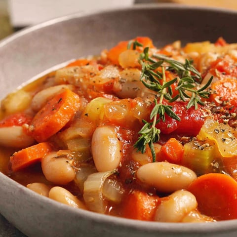 A bowl of stew with carrots, beans, and herbs.