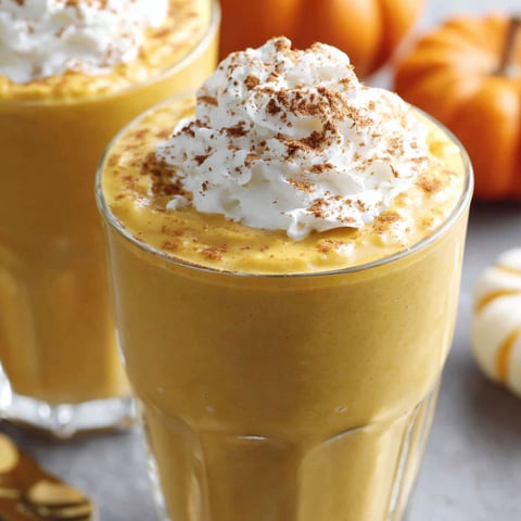 A glass of pumpkin smoothie with whipped cream on top.