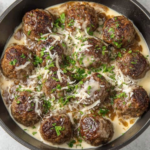A bowl of meatballs covered in cheese and herbs.
