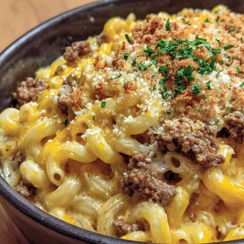 A bowl of macaroni and cheese with meat on top.