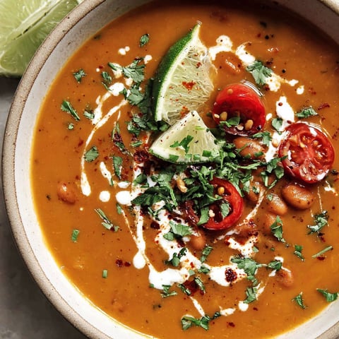 A bowl of spicy pinto bean soup with lime wedges and cilantro.