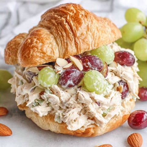 A chicken salad sandwich with grapes on top.