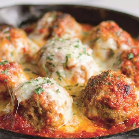 A plate of meatballs covered in cheese and tomato sauce.