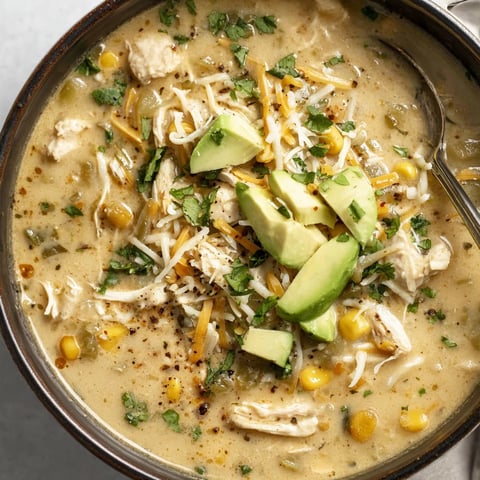 A bowl of soup with chicken, avocado, and corn.